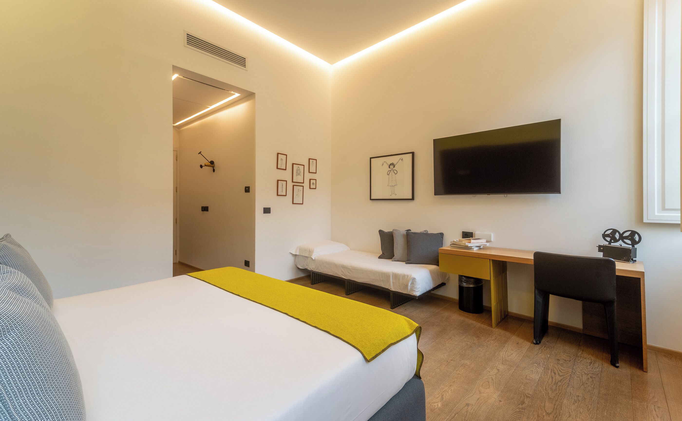 A hotel room with a bed, a desk, a chair, a TV, and a door.