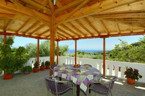 A covered outdoor patio with a table set for two, surrounded by potted plants and overlooking a scenic landscape.