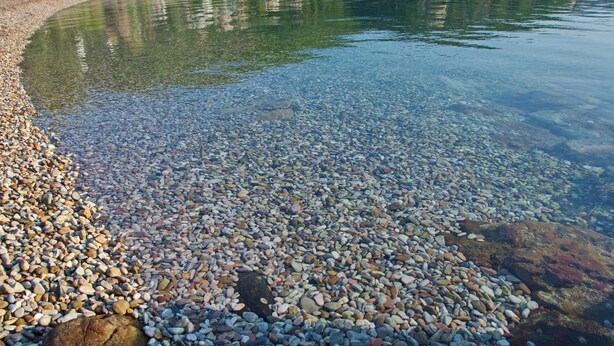 A pebbled beach with clear water, surrounded by greenery and houses in the background. - Limani Cottage (Alonissos)