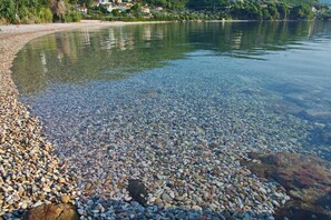 A pebbled beach with clear water, surrounded by greenery and houses in the background. - Limani Cottage (Alonissos)