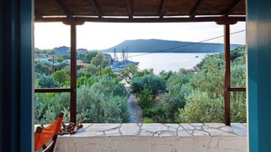 A covered outdoor area with a stone wall and a view of a body of water, boats, and distant hills. - Limani Cottage (Alonissos)