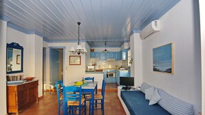 A compact kitchen with blue cabinets, a dining area with blue chairs, a sofa, and a TV. - Limani Cottage (Alonissos)