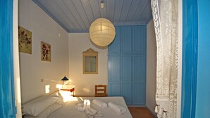A bedroom with a bed, a nightstand, a lamp, a window, and a door. - Limani Cottage (Alonissos)