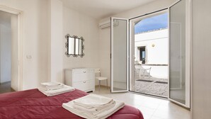 Una camera da letto con un letto, una cassettiera, uno specchio e una porta a vetri scorrevoli che dà su un patio esterno.