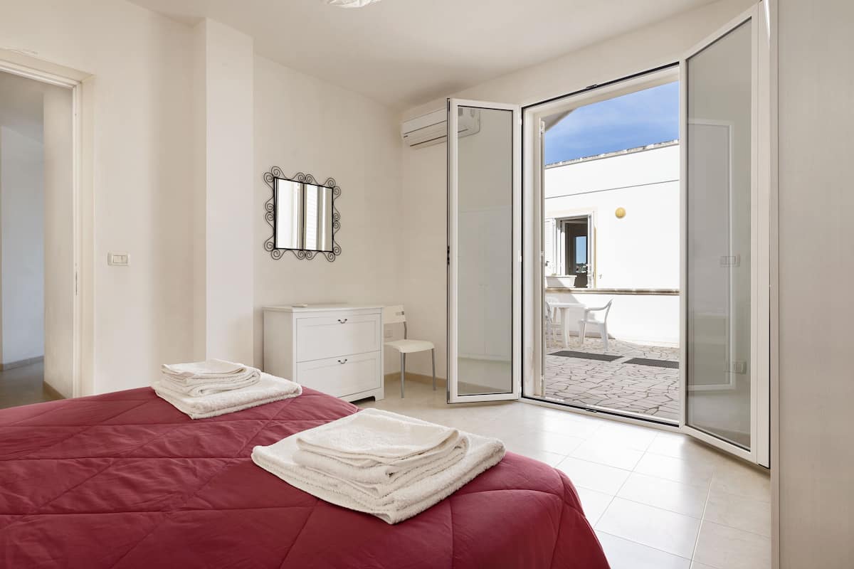 A bedroom with a bed, a dresser, a mirror, and a sliding glass door leading to an outdoor patio.