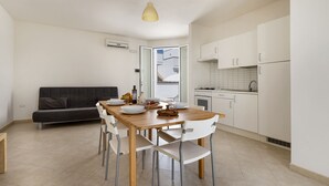 Una cucina compatta con mobili bianchi, un tavolo da pranzo con sedie e un divano sullo sfondo.