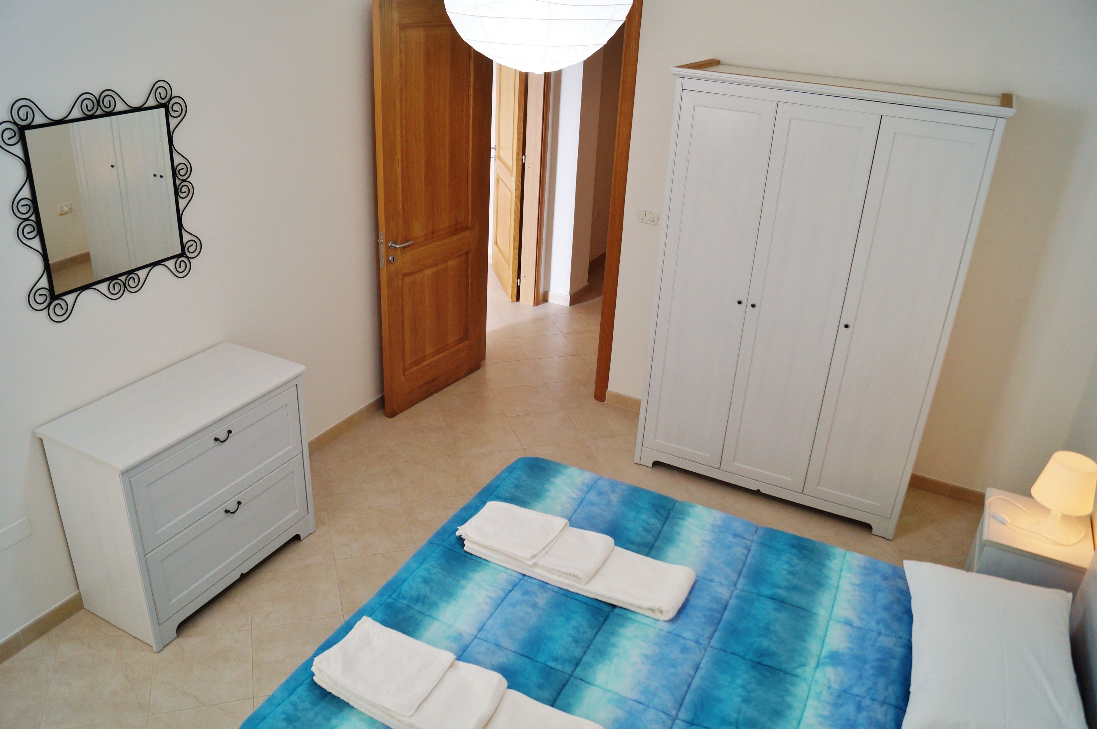Quarto com cama, mesa de cabeceira, penteadeira, guarda-roupa e espelho.