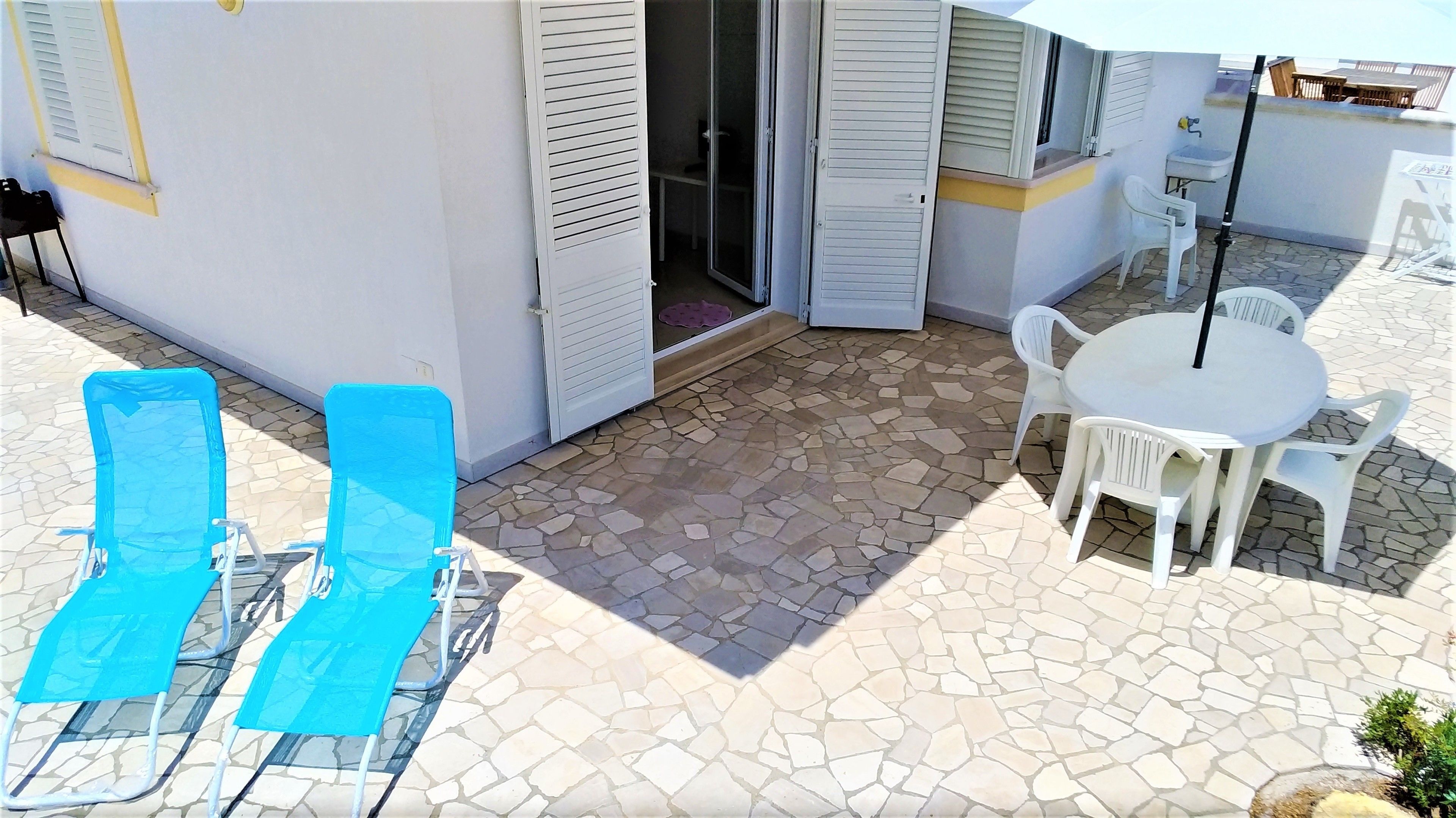Un patio con dos sillones azules, una mesa blanca con cuatro sillas y un lavamanos pequeño.
