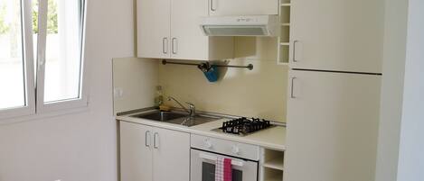 Una cocina compacta con armarios blancos, estufa, horno y ventana.