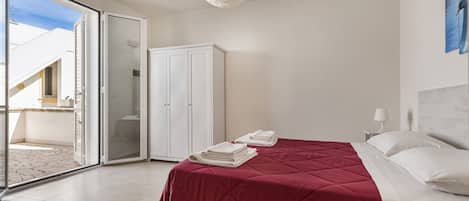 A bedroom with a bed, a wardrobe, and a sliding glass door leading to a balcony.