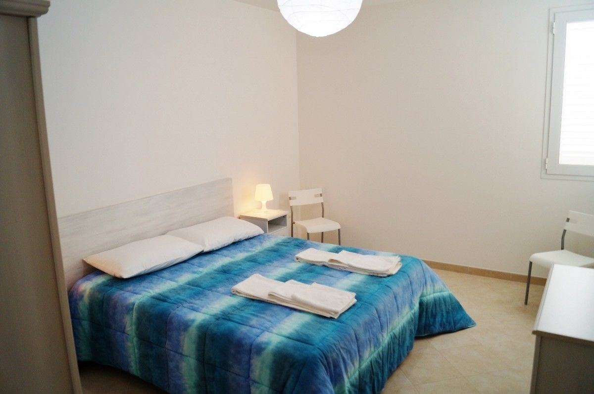 A bedroom with a bed, a nightstand, a chair, and a desk.