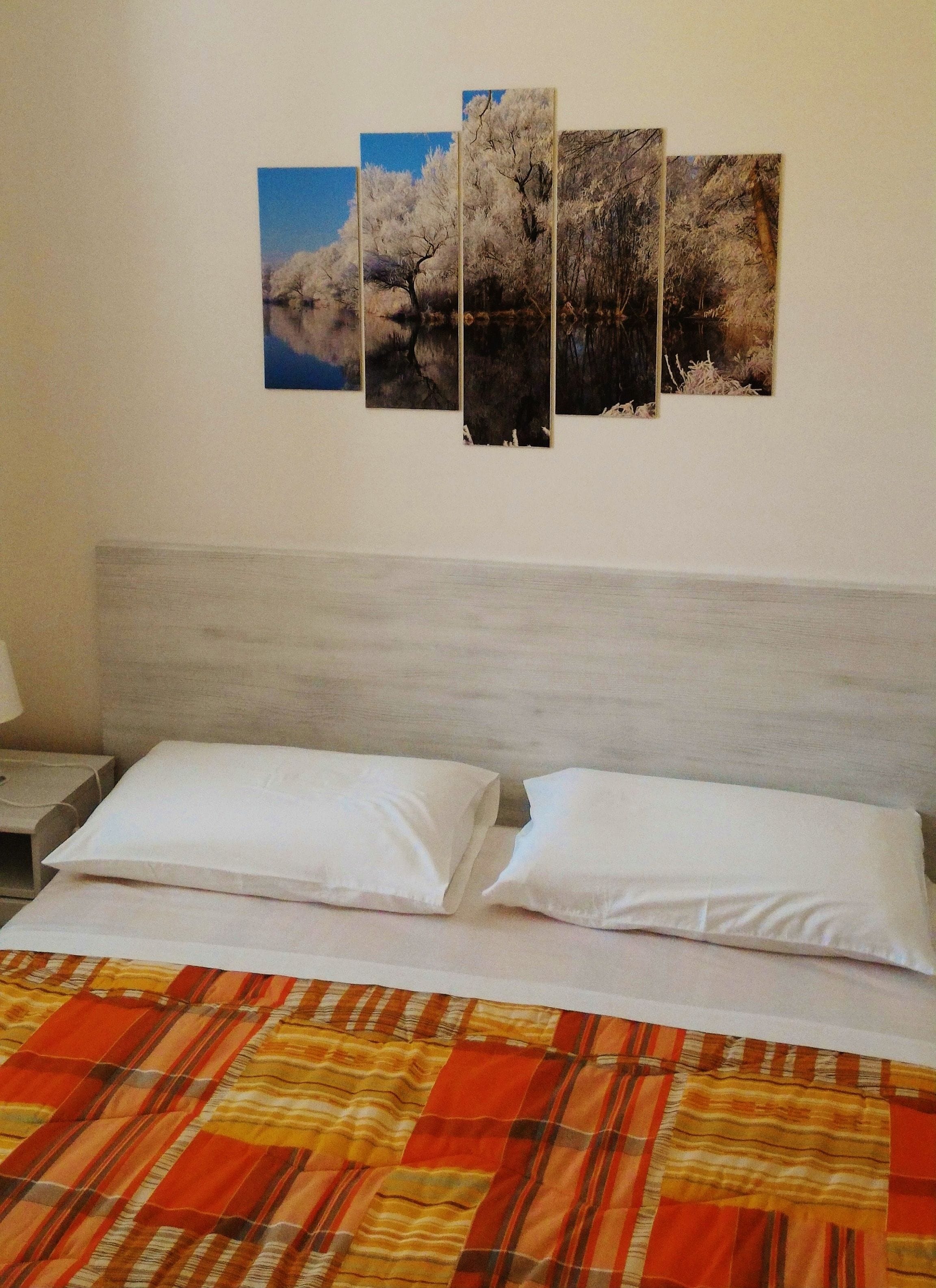 Ein Hotelzimmer mit einem Bett, weißen Kissen, einer gestreiften Decke und einer Wand mit vier gerahmten Bildern.