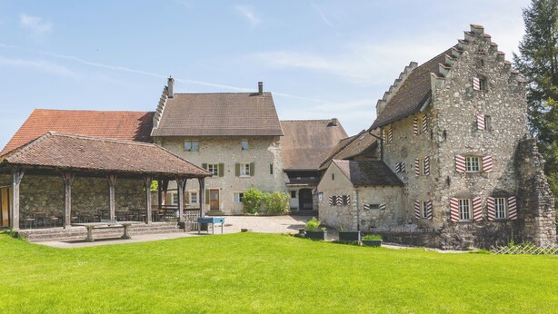A stone building with a red-tiled roof, a covered patio, and a grassy courtyard. - Youth Hostel Brugg (Brugg)