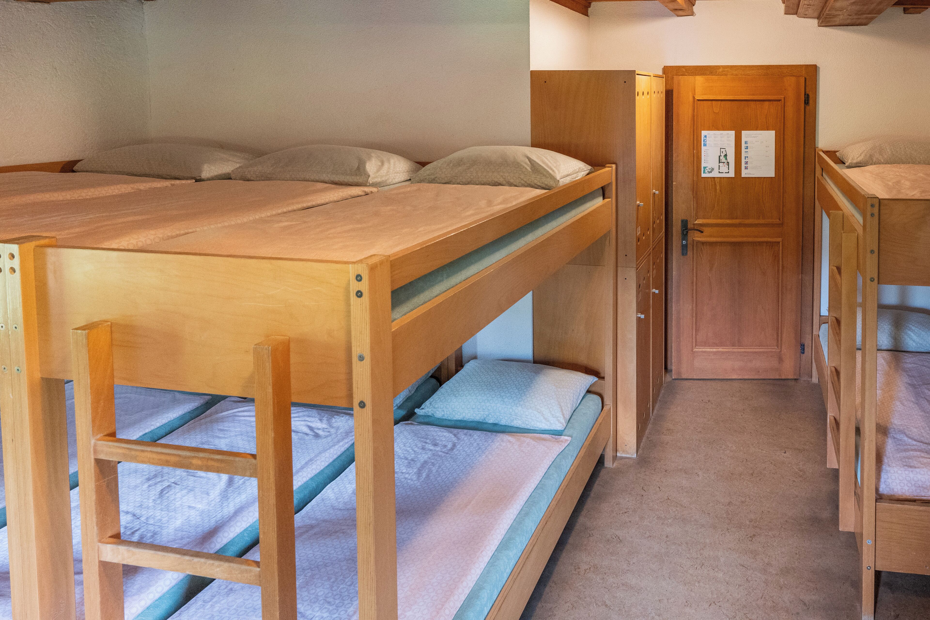 Une pièce avec des lits superposés, une porte en bois et un petit placard.