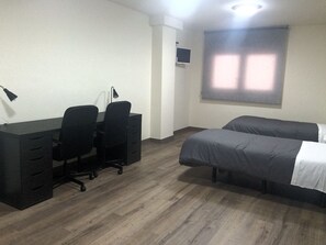 Una habitación con escritorio, dos sillas, cama y ventana con persianas.