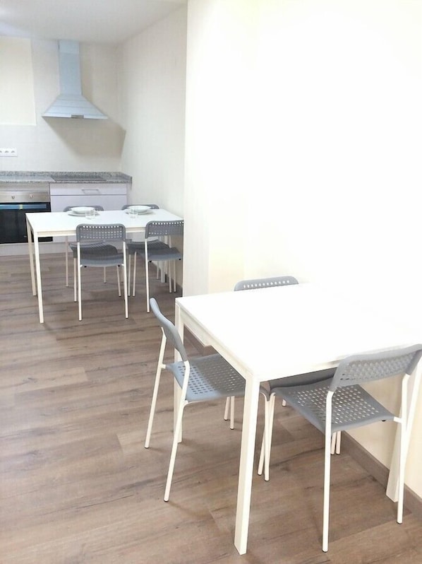 Una cocina moderna con armarios blancos y una campana extractora de acero inoxidable. Hay un comedor con una mesa blanca y cuatro sillas.