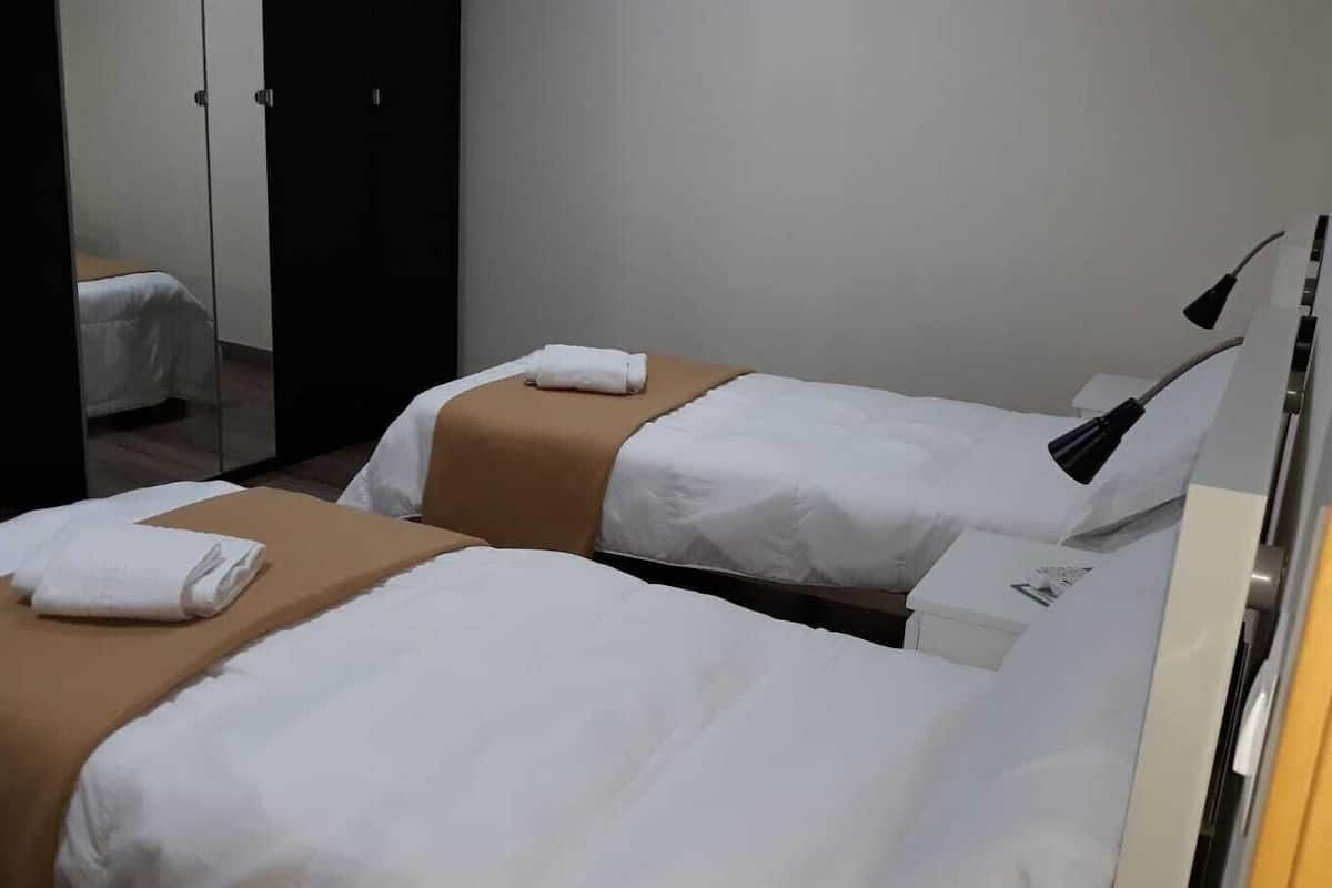 A hotel room with two beds, each with white bedding and brown headboards. There is a mirror on the wall and a lamp on the side.