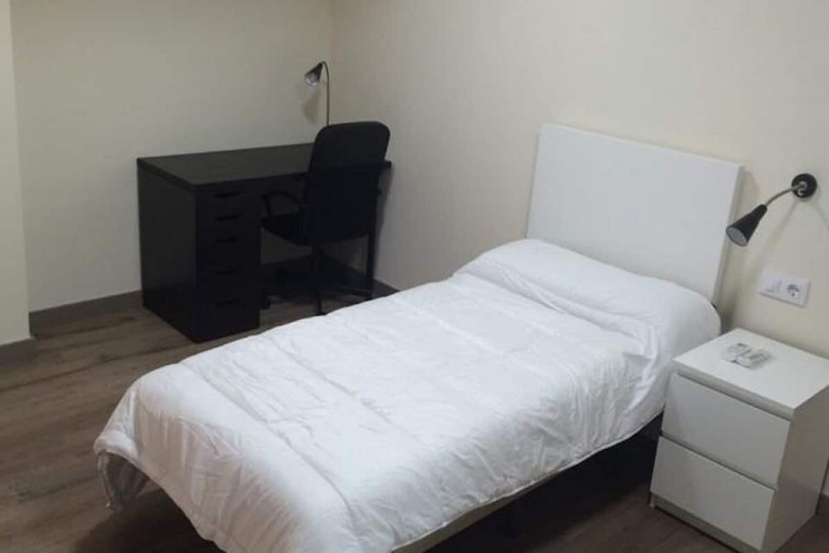 A small, neatly arranged bedroom with a single bed, a desk, and a chair.