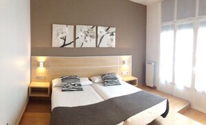 A double bed with a grey blanket, two black and white pillows, and a headboard with wall-mounted lights. There are three wall-mounted artworks above the bed. - Pensión Kursaal (San Sebastián)