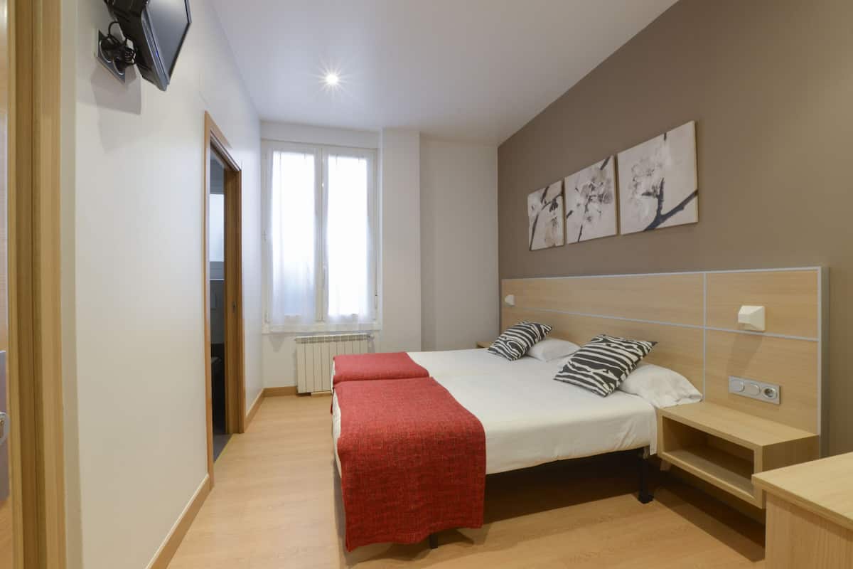 A bedroom with a large bed, a bedside table, a red throw blanket, and artwork on the wall.