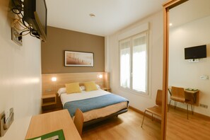A hotel room with a bed, bedside tables, a desk, a chair, a TV, and a window. - Pensión Kursaal (San Sebastián)