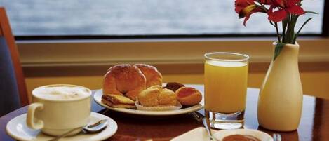 A breakfast setting with croissants, a glass of orange juice, and a cup of coffee on a table by a window.