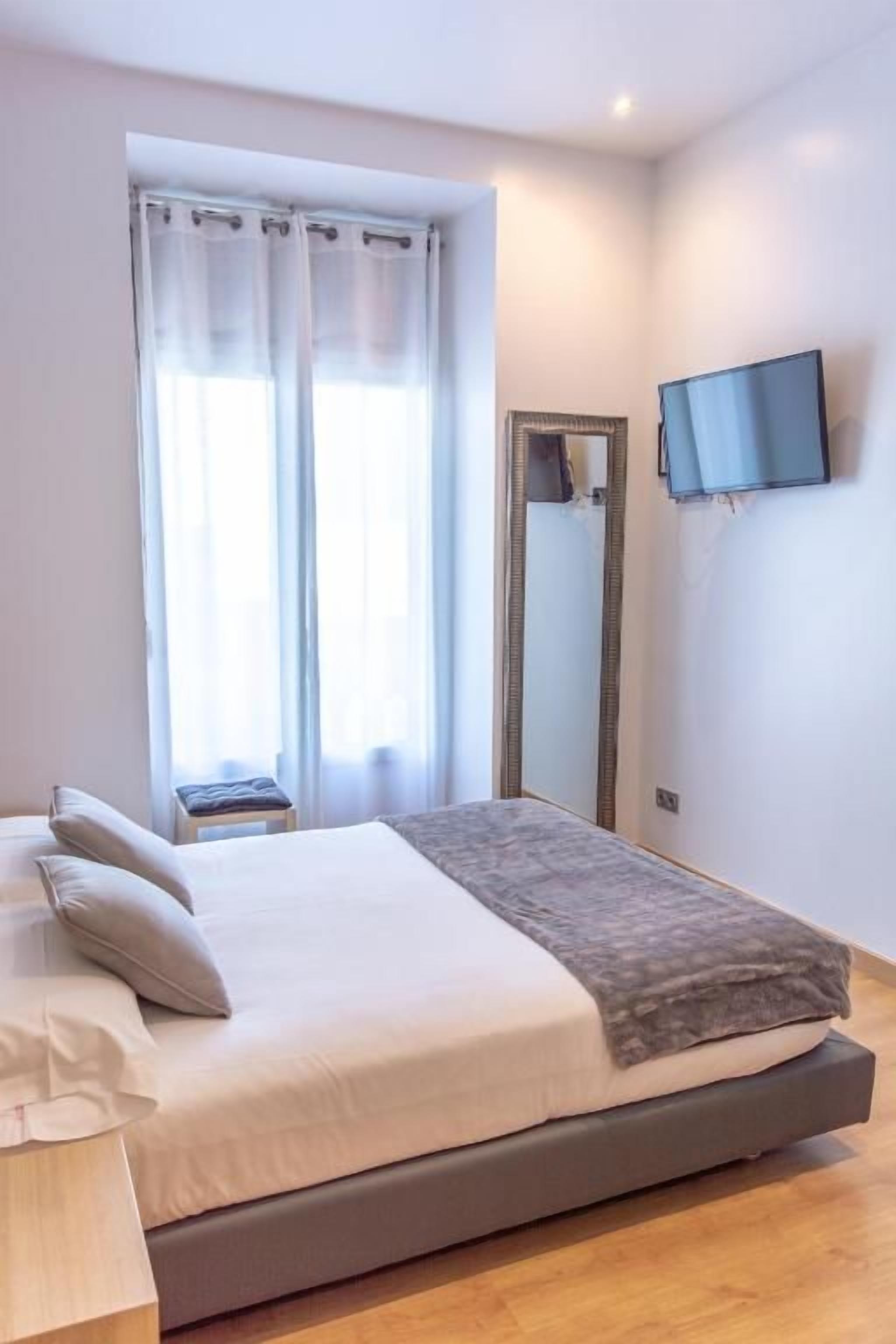 A bedroom with a bed, a television mounted on the wall, and a window with curtains.