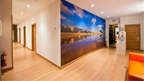 A hotel corridor with a large cityscape mural on the wall, wooden flooring, and a fire extinguisher on the left. - Pensión Kursaal (San Sebastián)