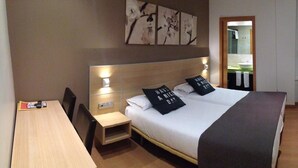 A hotel room with a large bed, a bedside table, a desk, and a mirror. - Pensión Kursaal (San Sebastián)