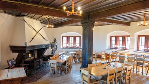 A rustic dining hall with wooden tables and chairs, a stone fireplace, and arched windows. - Youth Hostel Mariastein (Metzerlen)