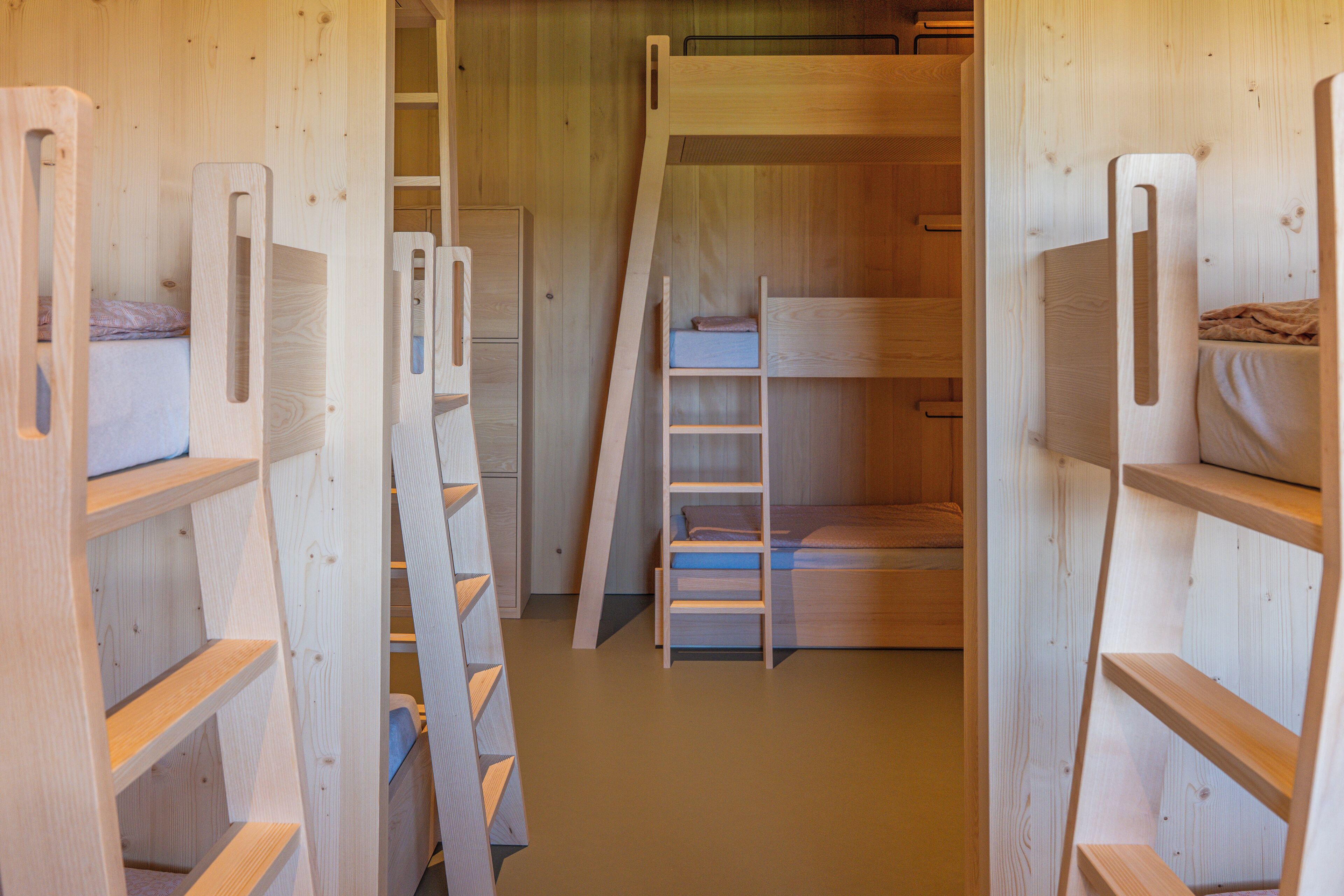 Habitación con literas de madera, una escalera y estanterías empotradas.
