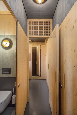 Un interior de madera con un inodoro, un lavabo y una puerta que da a otra habitación.