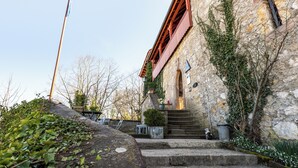 A stone building with a wooden staircase leading to a door, surrounded by greenery. - Youth Hostel Mariastein (Metzerlen)