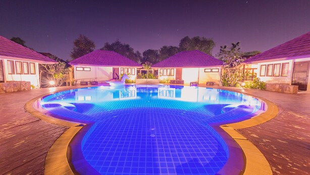 A swimming pool with a tiled deck surrounding it, connected to a building with a purple roof. - Baan Suan Nuanta (Samut Songkhram)