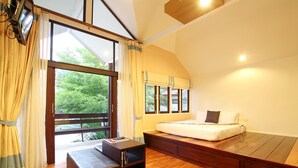 A bedroom with a bed, a bench, a small table, and large windows. - Baan Suan Nuanta (Samut Songkhram)