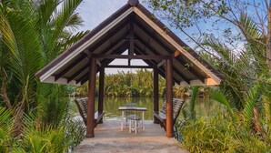 A gazebo with a table and chairs, surrounded by water and greenery. - Baan Suan Nuanta (Samut Songkhram)