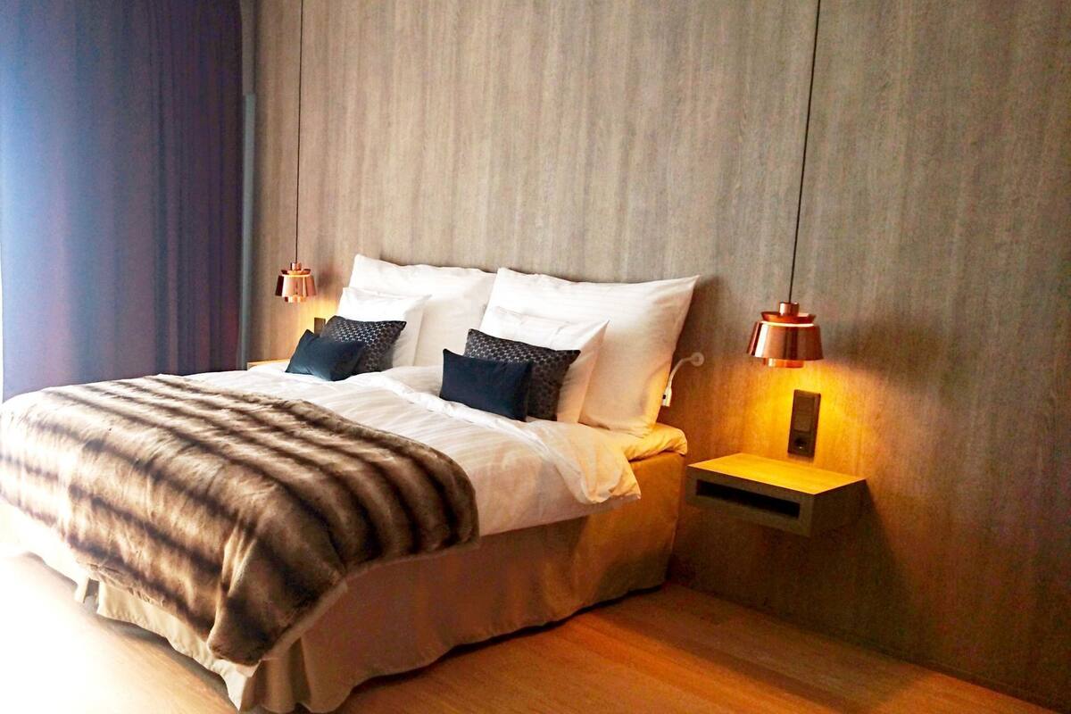 Een netjes opgemaakt bed met een gestreept dekbed, twee nachtkastjes met lampen, en een houten hoofdbord.