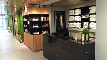 A hotel reception area with a wooden counter, shelves with toiletries, and a wall displaying folded towels.