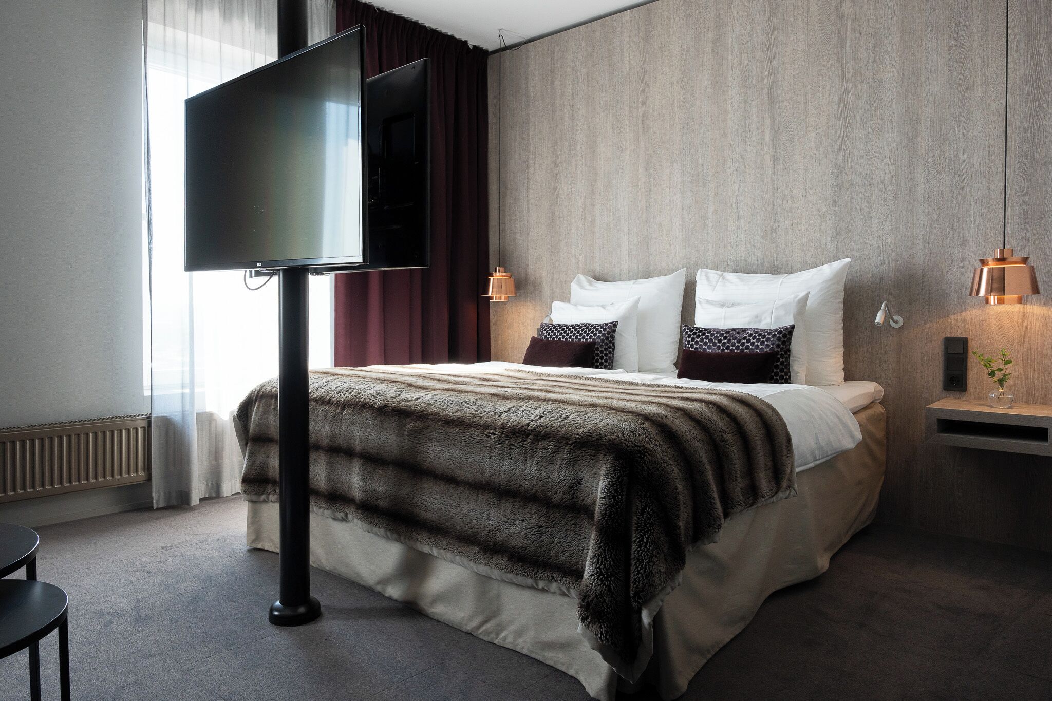 Habitación de hotel moderna con una cama grande, un televisor de pantalla plana, una mesita de noche con lámpara y vistas al exterior.