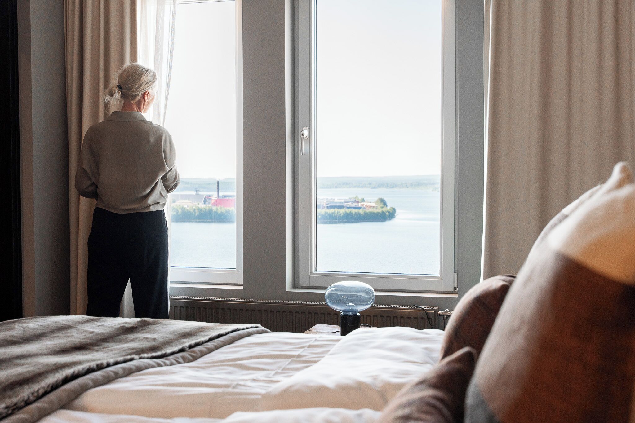 Una habitación con una cama, un ventanal con cortinas y vista a un cuerpo de agua.