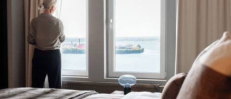 Una habitación con una cama, un ventanal con cortinas y vista a un cuerpo de agua.