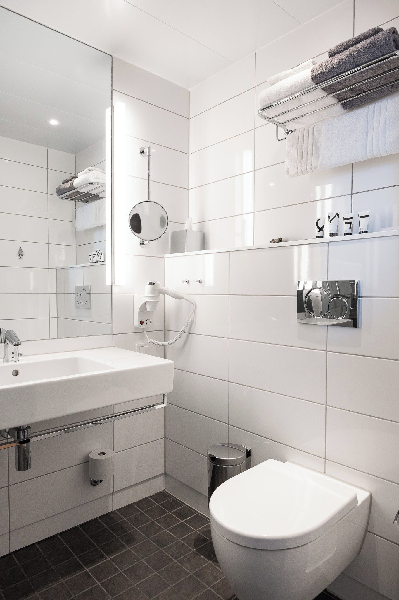 Un baño moderno con un lavamanos blanco, un inodoro, un perchero para toallas y un espejo.