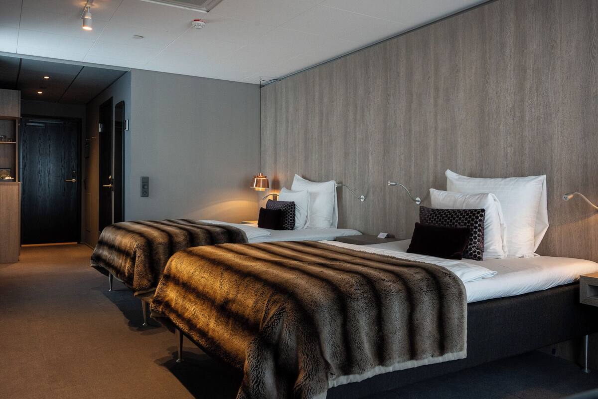 Een moderne hotelkamer met twee bedden, een houten accentmuur en een gang naar een andere kamer.