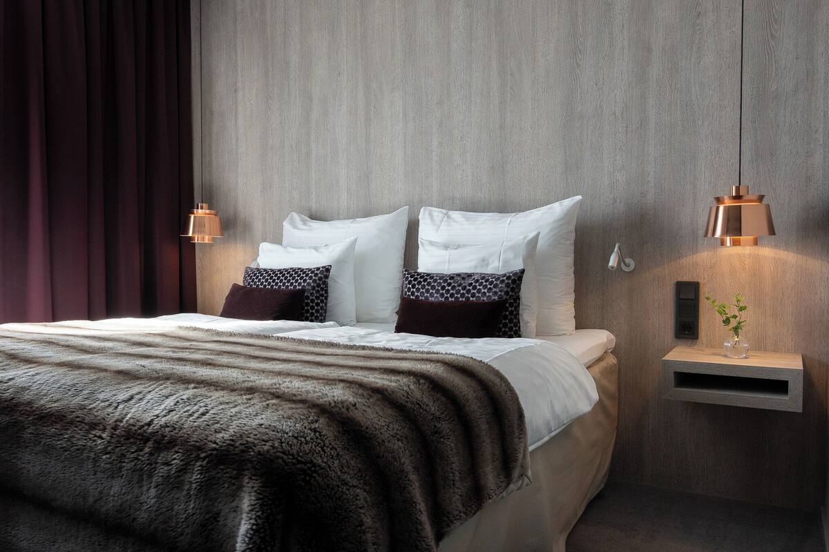 Een moderne slaapkamer met een groot bed, twee bedlampen, een nachtkastje met een vaas en een houten hoofdbord.