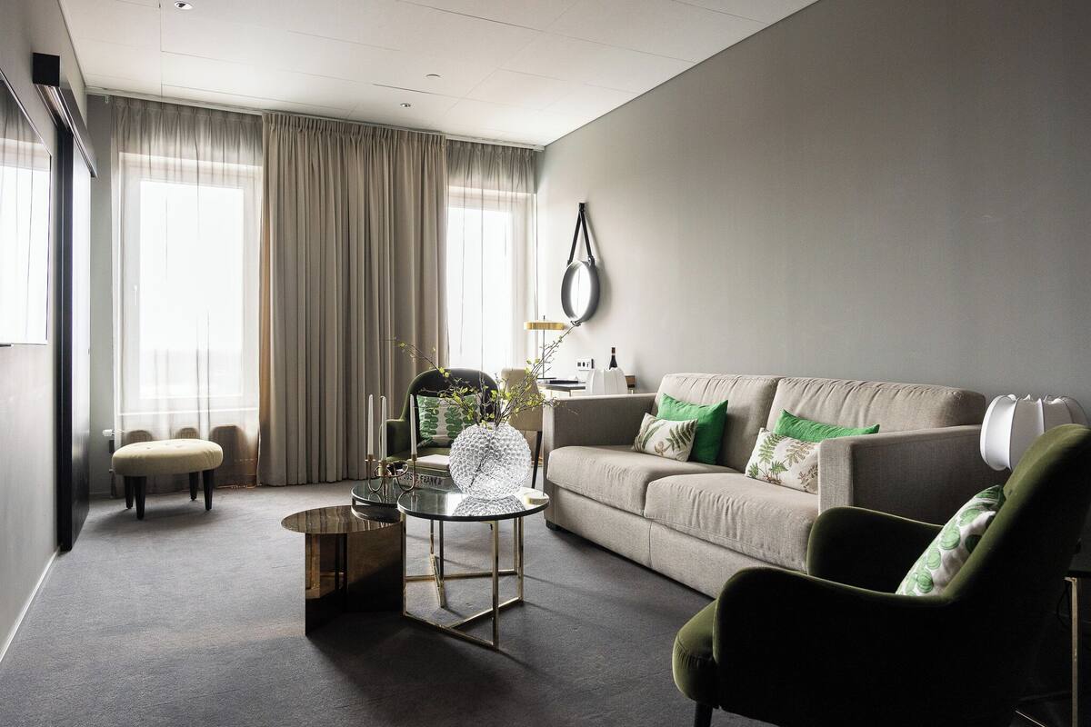 Een moderne woonkamer met een bank, fauteuil, voetenbankje, een glazen salontafel en een lamp.
