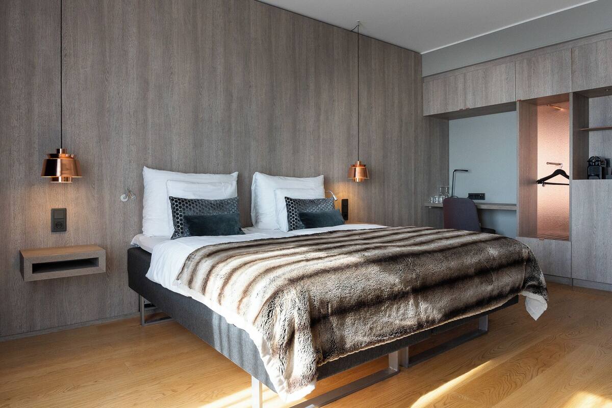 Een moderne slaapkamer met een houten wand, een bed met een gestreepte deken, bedlampen en een inbouwkast.