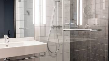 Un baño moderno con ducha de vidrio, lavamanos blanco y piso de baldosas oscuras.