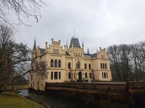 A large, historic building with multiple towers and arched windows, surrounded by a moat and trees. - Am Lindenhof Bunde (Bunde)