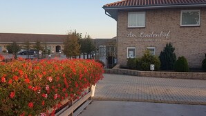 Un hotel chiamato Am Lindenhof con un ingresso pavimentato e un aiuola con fiori rossi.