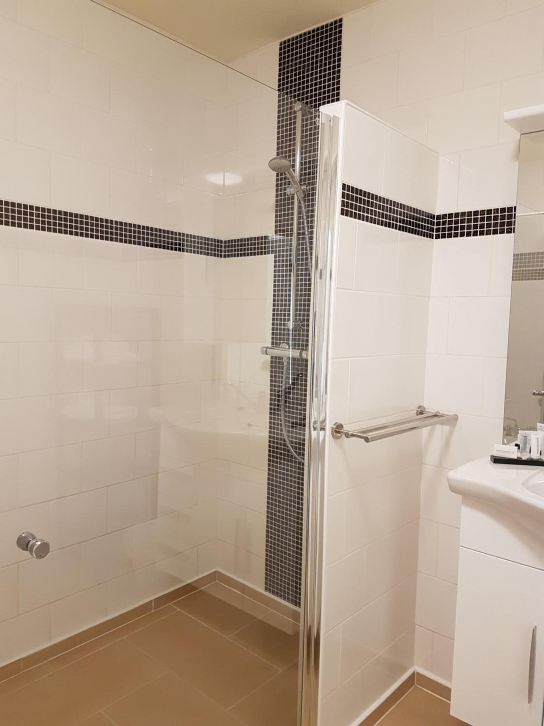 A bathroom with a glass shower enclosure, white tiled walls, and a beige floor.